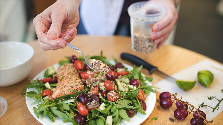 Hand spooning seeds on salad 