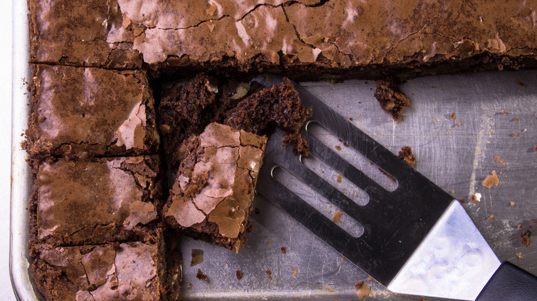 brownies baked in a metal pan with peices served and a metal spatula