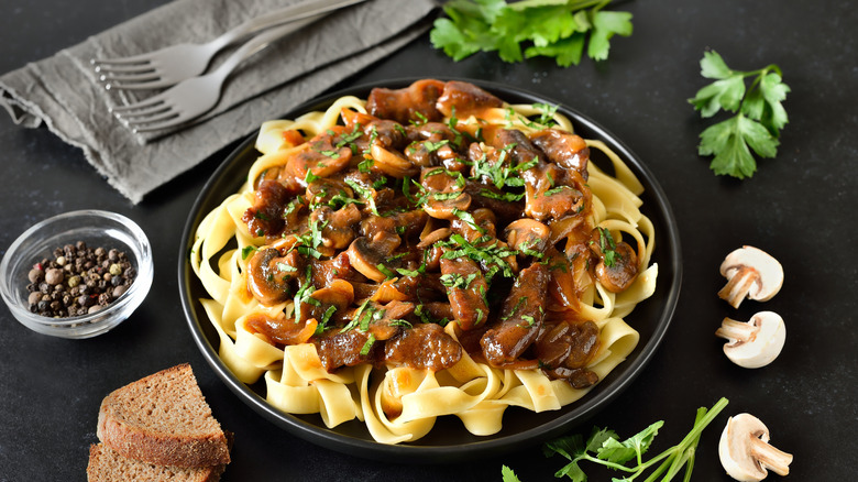 Beef stroganoff with mushrooms over egg noodles, on a black table.