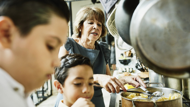A woman cooking in the kitchen, 2 children in the foreground.