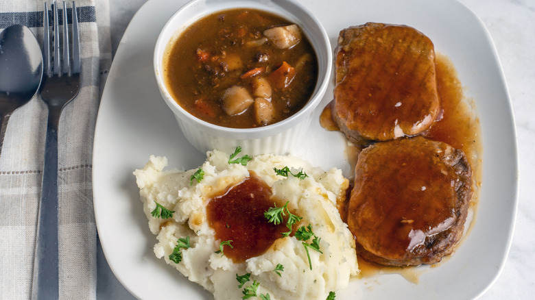 Salisbury steaks on a white plate with mashed potatoes and gravy, overhead on a white table.