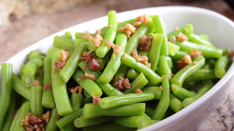 Green beans topped with crispy bacon in white oval bowl