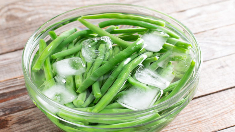 Blanched green beans in glass bowl filled with ice water