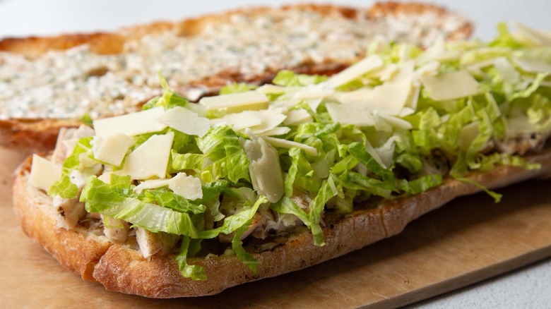Toasted bread covered in creamy dressing, chopped chicken, cheese, and lettuce