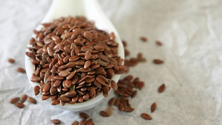 Close up of a spoon of flaxseeds on a white background.