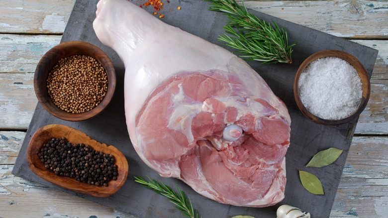 Raw bone-in pork leg on platter with salt and pepper corns.