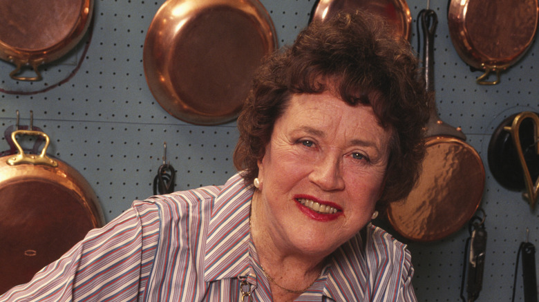 Julia Child with pots and pans hanging the background