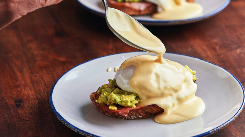spooning hollandaise sauce onto eggs benedict