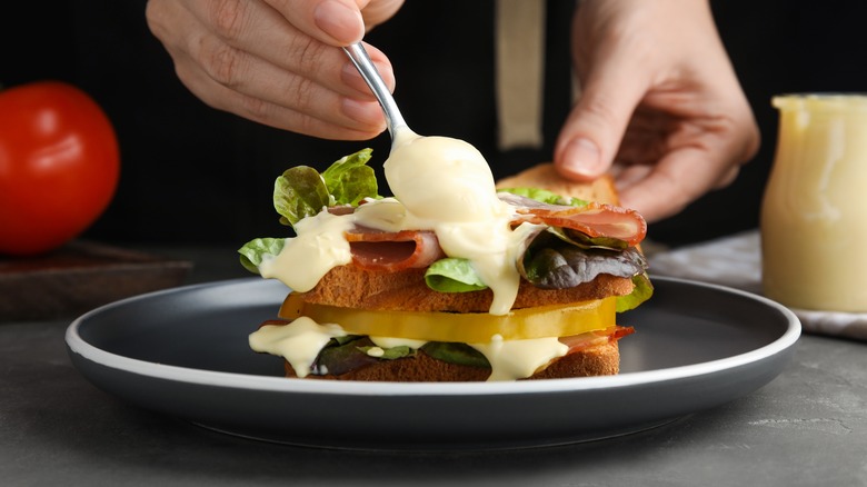 hands spooning mayonnaise on sandwich on black plate