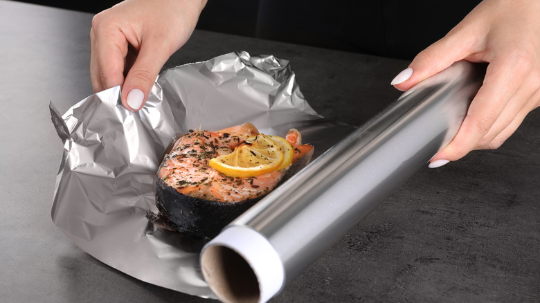 Person wrapping salmon in aluminum foil
