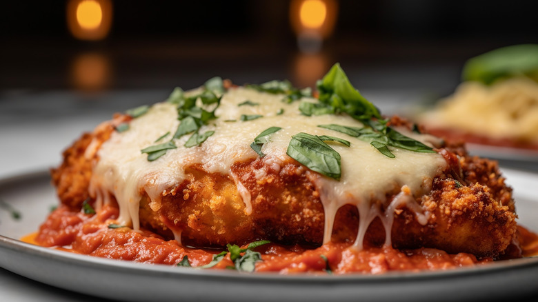 A breaded chicken cutlet topped with melted parmesan cheese and herbs, on a bed of red sauce
