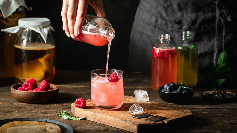 Hand pours pink kombucha into a glass on wooden board