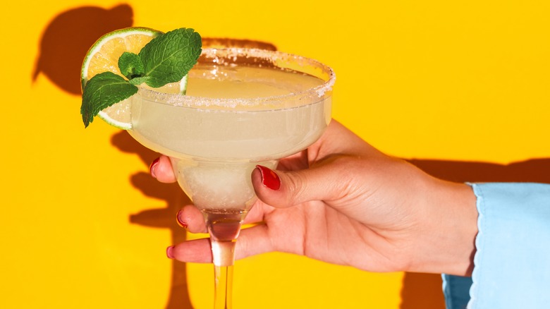 Hand holding margarita on yellow background