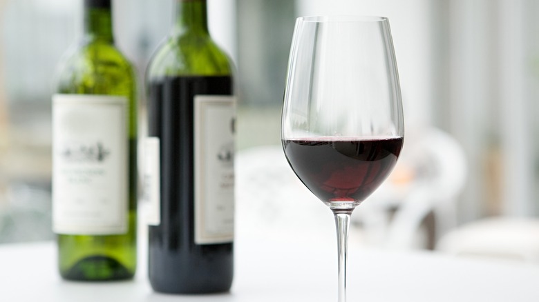 A glass of red wine with two wine bottles