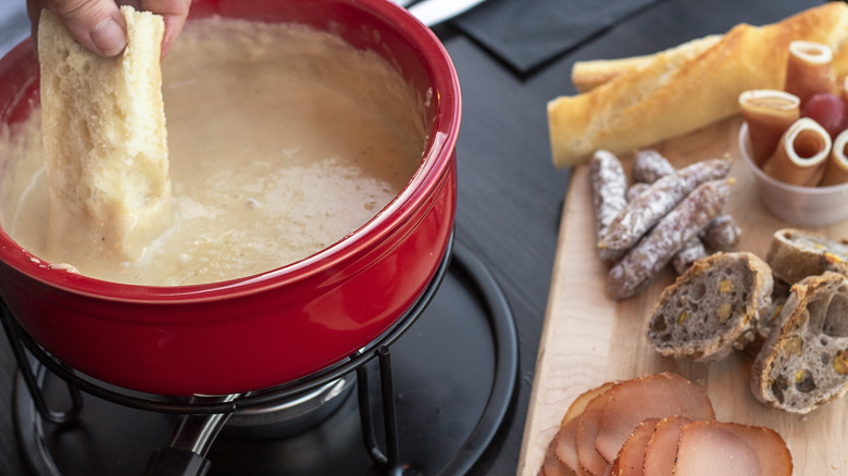 Hand dipping bread into fondue