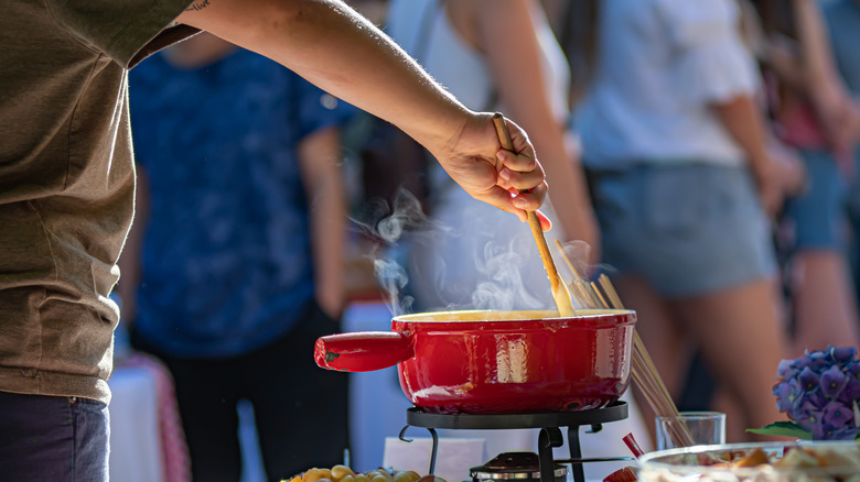 Person stirring fondue with tool