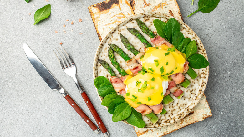 Eggs Benedict with green asparagus wrapped in grilled bacon