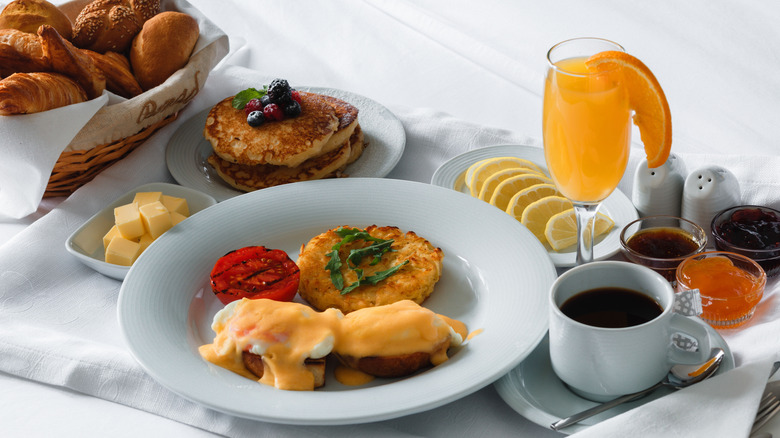 A brunch table with plates of eggs Benedict, pancakes, and fruit salad