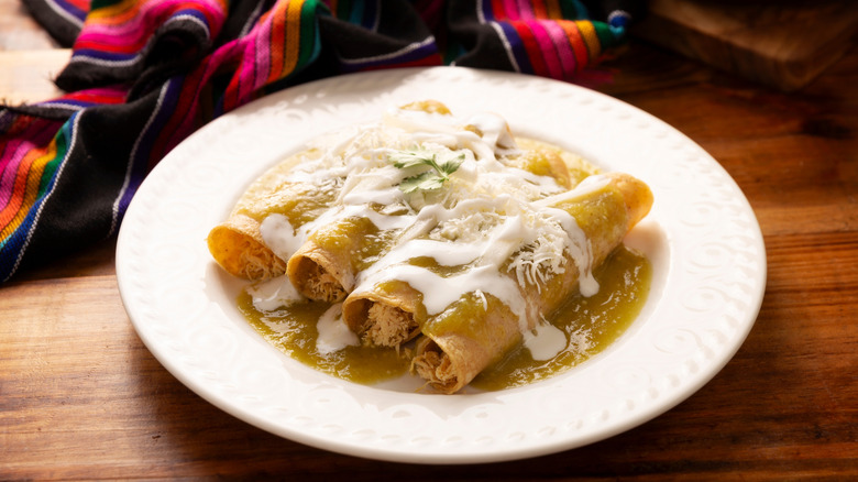 A plate of hot chicken enchiladas with a green chile sauce and melted cheese