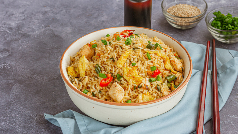 A bowl of chicken fried rice with red peppers, green onions, sesame, peas and egg ready to eat for dinner