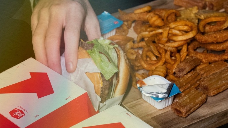 hand grabbing burger from Jack in the Box with curly fries