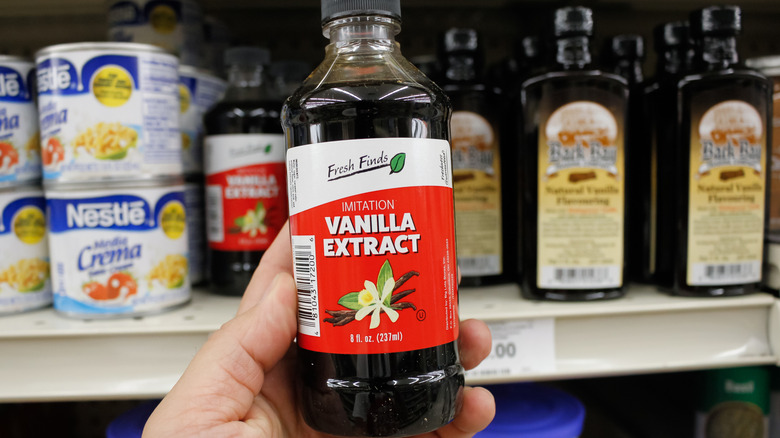 A person holding an 8-ounce bottle of Imitation Vanilla Extract in a grocery store