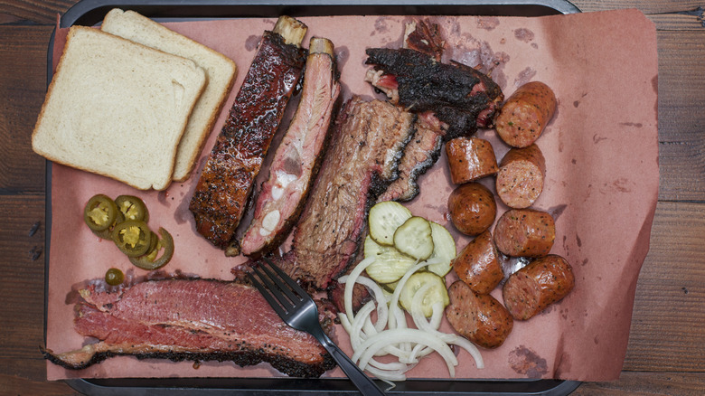 Tray of barbecued meats on a tray with white bread, pickles, onions, and jalapenos