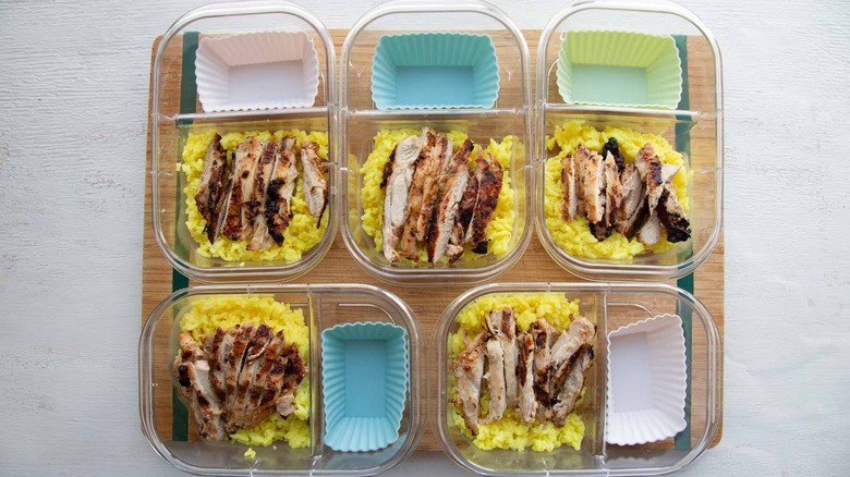 five meal prep containers with chicken, rice, and silicone muffin tin