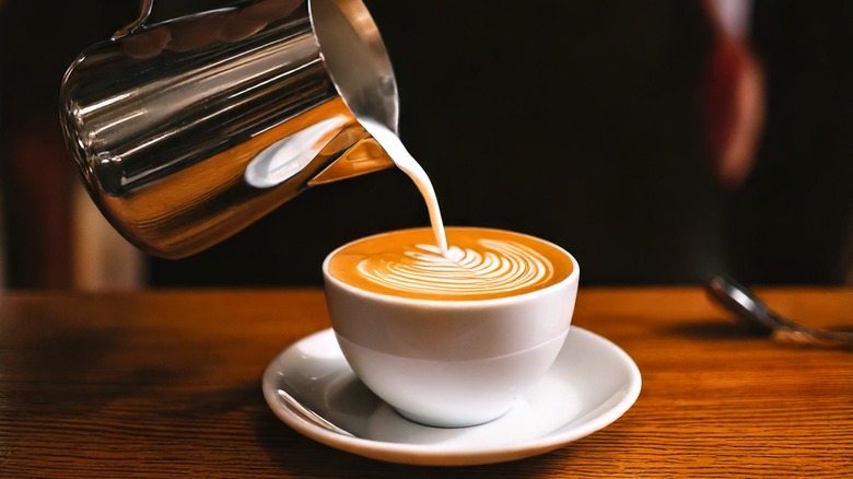 Milk foam is poured on top of a latte to create a pattern on top