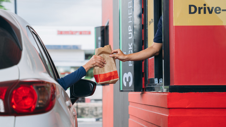 Fast food employee handing bag to customer in car at drive-thru