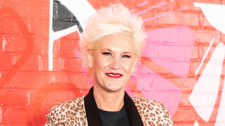 Anne Burrell with her trademark spiky blonde hair, wearing a leopard print coat and black t-shirt