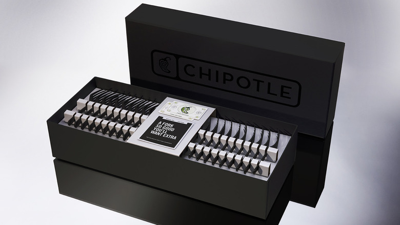 A black box with a black Chipotle logo on its lid, opened to show 53 black forks on their sides, with two cards for free food in the middle, and the tagline 
