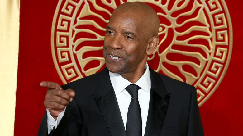 Denzel Washington pointing off-camera in a black suit at a red carpet event