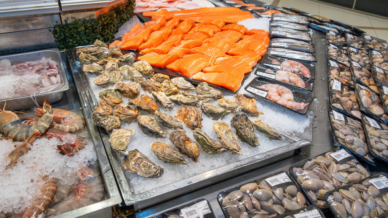 A grocery store seafood counter with visible salmon, clams, shrimp, and oysters.