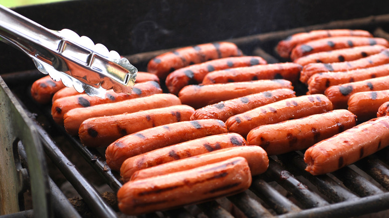 tons of hot dogs on grill with tongs