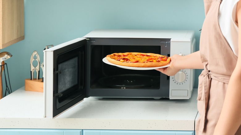 woman taking pizza from microwave