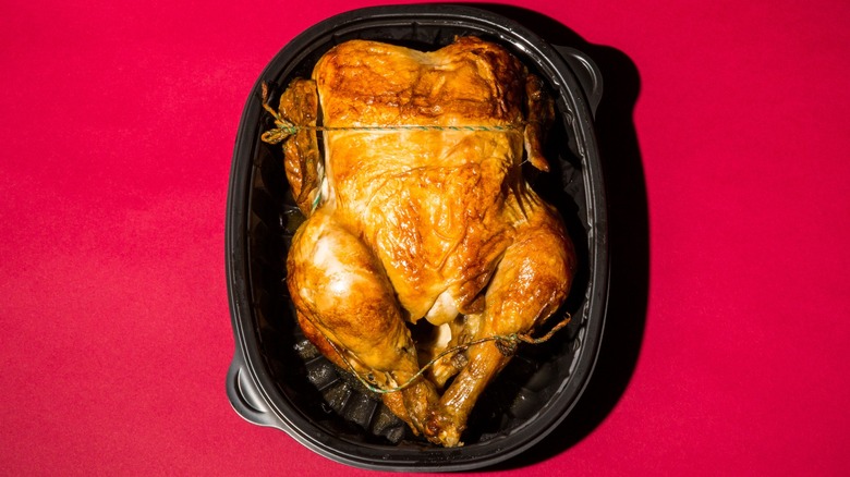 Overview of a cooked rotisserie chicken trussed with twine on a red background