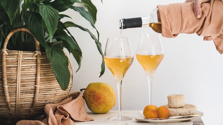 hand pouring bottle of orange wine into glasses