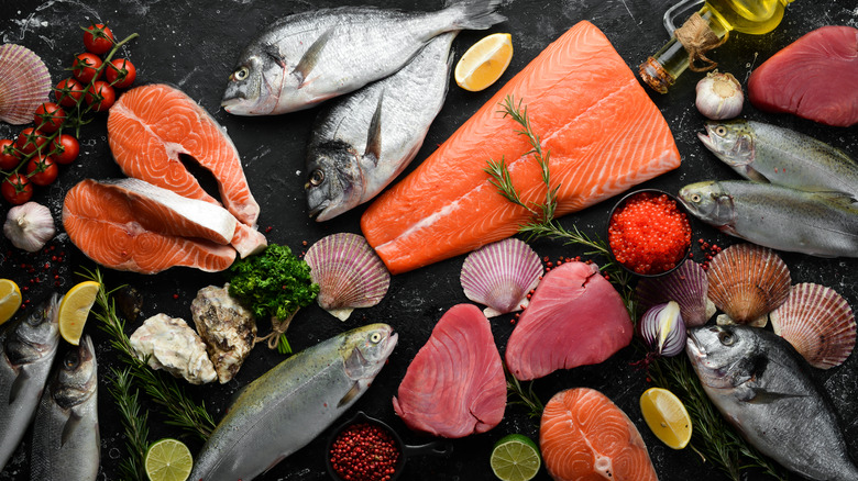 Variety of whole and cut fish, caviar, and shells with lemon and lime wedges and herbs