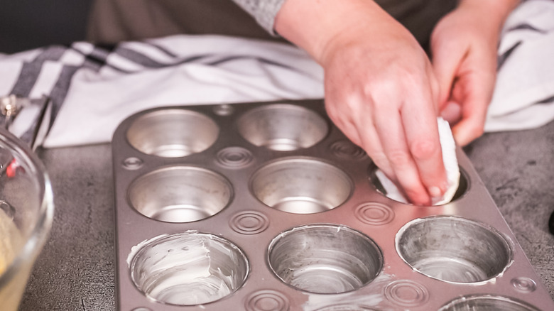 person greasing muffin tin with butter