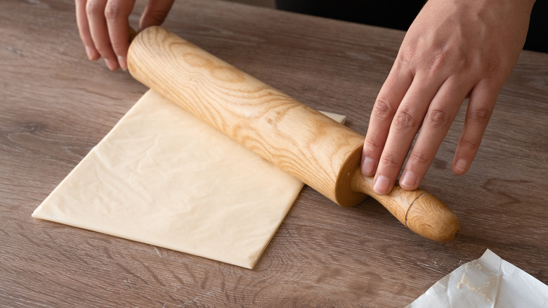 A woman rolling out butter wrapped in parchment paper with a rolling pin
