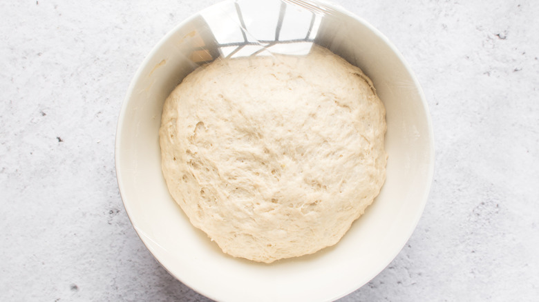 Dough resting in a bowl covered with plastic wrap