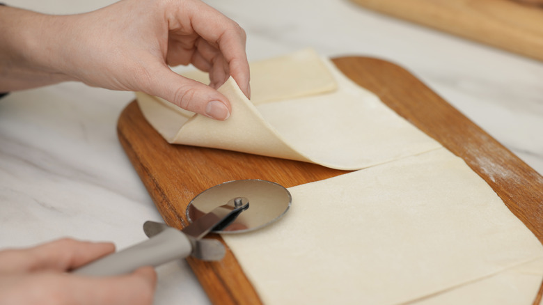 A woman cutting dough on a wooden board with a pizza cutter