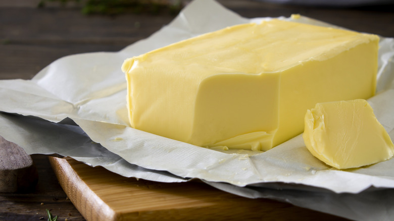 A block of butter on a paper placed on a wooden board