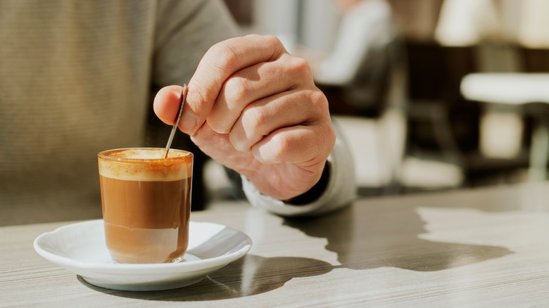 A closeup of a person stirring a cortado coffee