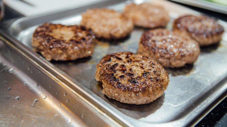Cooked beef burger patties on a baking sheet
