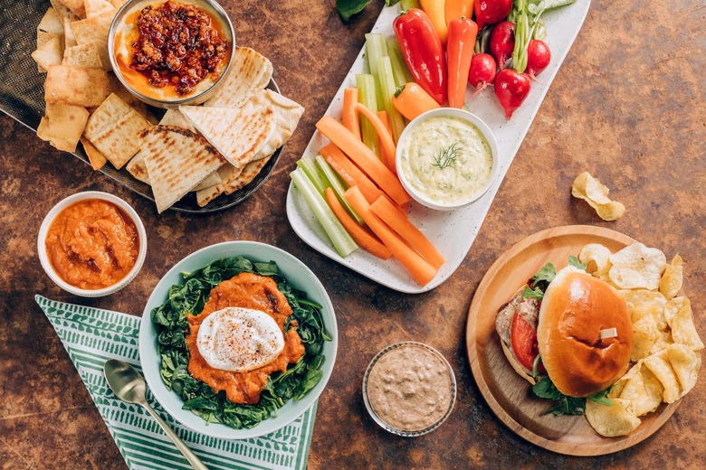 An array of homemade condiments: bacon ketchup & greens w/ poached egg; crudite w/ aioli; burger