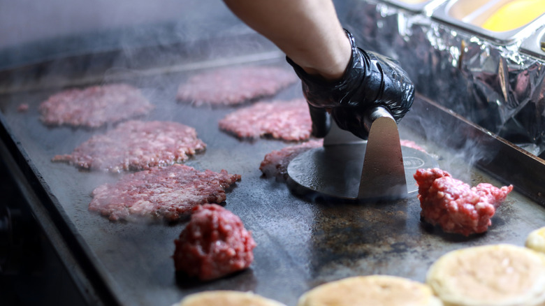 Smashing raw burger patties against a hot griddle