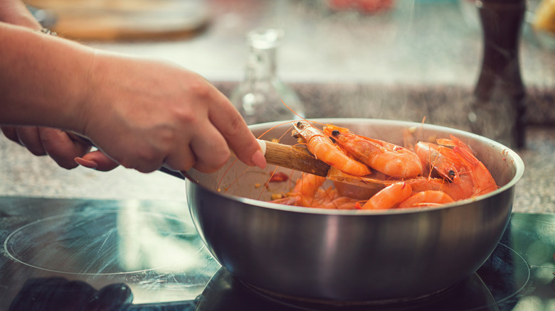 Person preparing shrimp scampi in a pan with white wine