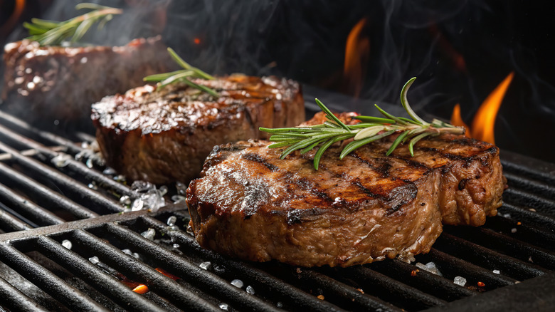 Steak cooking on grill with rosemary